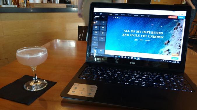 A coupe cocktail glass sits next to an open laptop.