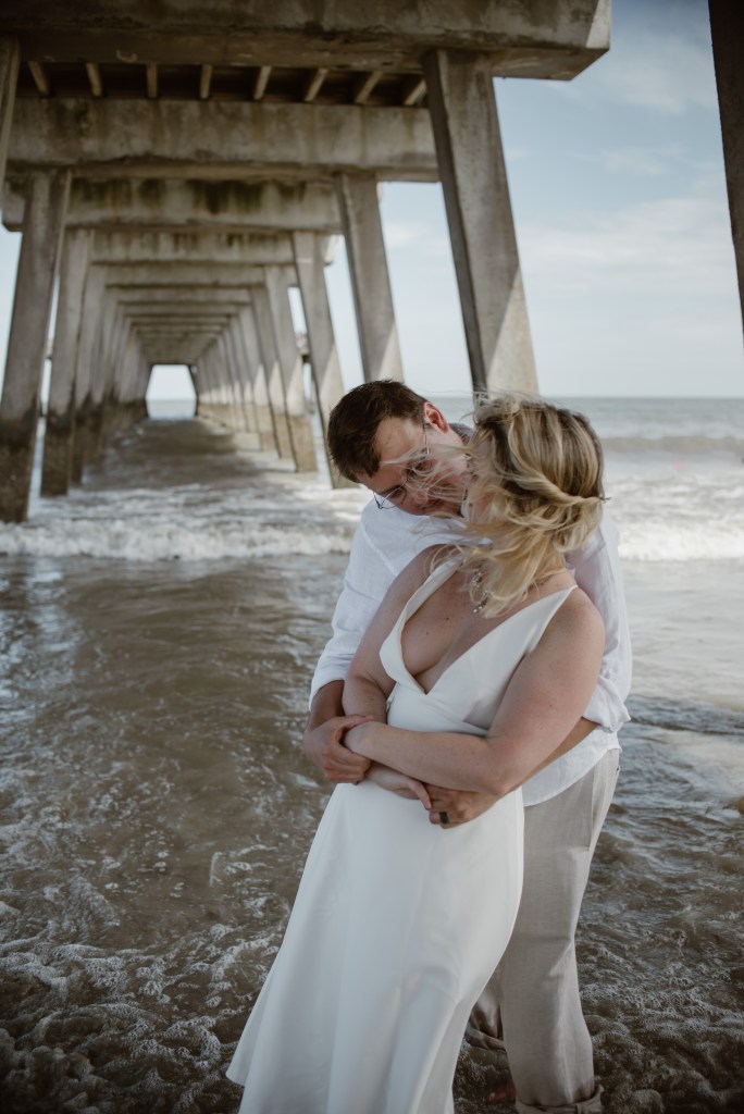 A couple dancing nuder a pier at the beach.