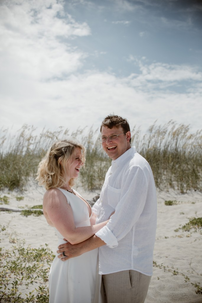The happy couple laughs after getting married on the beach.